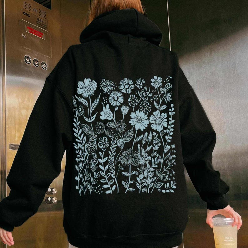 May include: Black hoodie with a light blue floral design on the back. The design features a variety of flowers and leaves.