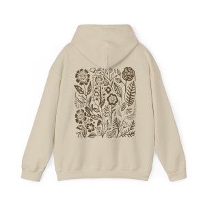 K&ouml;nnte beinhalten: Ein beiger Hoodie mit einem braunen Blumendruck auf der R&uuml;ckseite. Der Druck zeigt eine Vielzahl von Blumen, Bl&auml;ttern und Stielen.