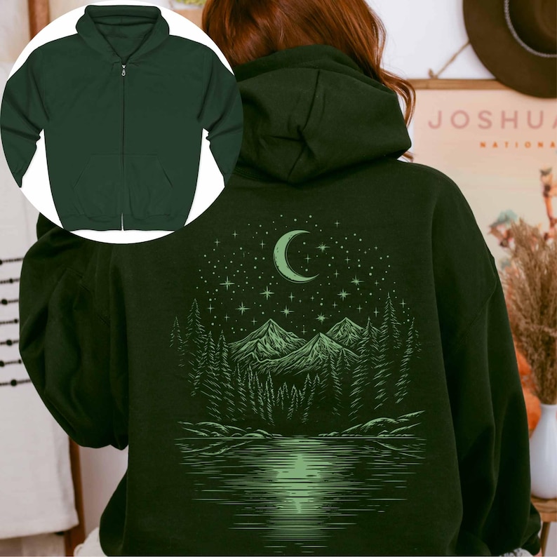May include: Dark green zip-up hoodie with a nature-themed graphic on the back. The design features a crescent moon, stars, mountains, trees, and a lake. The hoodie has a front zipper and a hood.