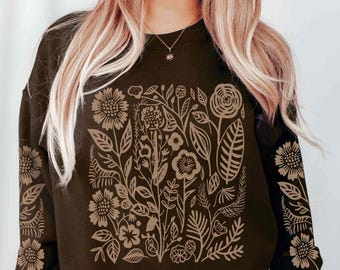 May include: A dark brown long-sleeve sweatshirt featuring a tan botanical print on the front and down the length of both sleeves. The graphic design consists of various stylized flowers, leaves, and stems arranged in a dense, intricate pattern.