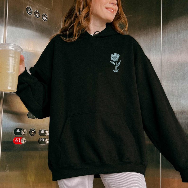 May include: A black hoodie with a small, light blue flower graphic on the left chest. The hoodie has a drawstring hood and a kangaroo pocket.