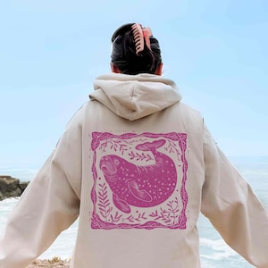 May include: A beige hoodie with a pink print of a manatee surrounded by floral designs on the back.
