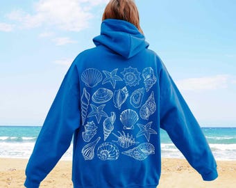 May include: A bright blue hooded sweatshirt featuring a white line-art graphic on the back. The design consists of a collection of various seashells and starfish arranged in a cluster, covering the centre portion of the garment's back panel.
