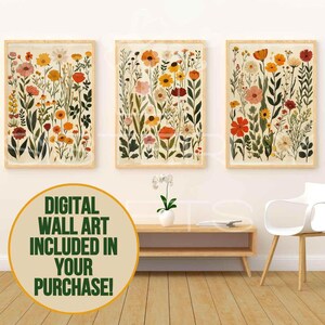 May include: Three framed floral art prints. Each print showcases a variety of colourful flowers in shades of red, orange, yellow, and pink, set against a cream background. The frames are a light wood colour. The text in the image says "DIGITAL WALL ART INCLUDED IN YOUR PURCHASE!"