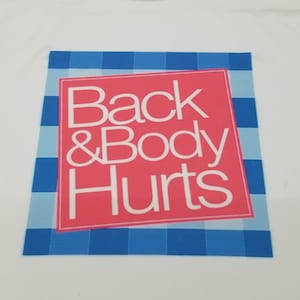 May include: White t-shirt with a blue and white checkered background and a red rectangle with the text "Back & Body Hurts" in white.