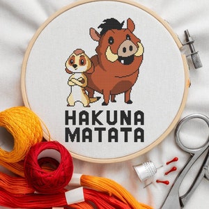 May include: A brown and yellow embroidery hoop with a cross-stitch design of Timon and Pumbaa from Disney's The Lion King. The design includes the phrase "Hakuna Matata".