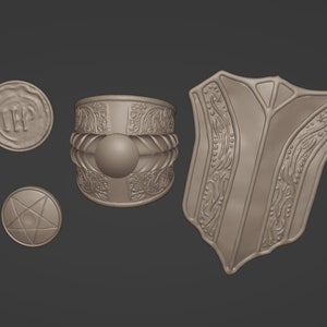 Puede incluir: Un conjunto de tres piezas de joyería de metal plateado. Las piezas incluyen un brazalete con un diseño ornamentado, un colgante circular con un diseño de estrella y un colgante circular con las letras "IEP" grabadas.