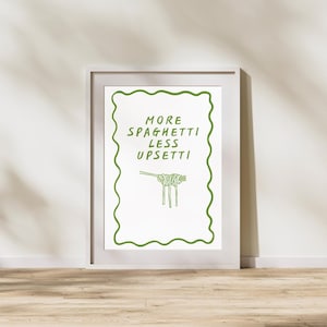 May include: A framed art print featuring the words "MORE SPAGHETTI LESS UPSETTI" in green, accompanied by a green spaghetti illustration. The artwork is set against a white background and framed in a white border. The theme is food and kitchen decor.