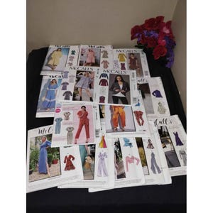 May include: A selection of McCall's sewing patterns displaying diverse designs for dresses, jumpsuits, and jackets. The patterns present colourful illustrations of the finished garments, with a range of styles and sizes. The patterns are arranged on a black surface.