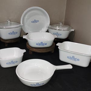 May include: A set of blue and white casserole dishes with a floral design. The set includes a large casserole dish, a smaller casserole dish, a round baking dish, and a frying pan.