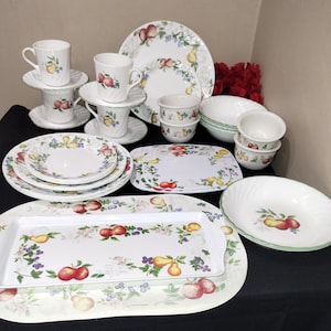 May include: A set of white dinnerware with a floral pattern featuring apples, pears, and berries. The set includes plates, bowls, cups, and saucers.
