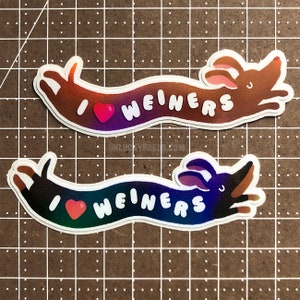 Op de afbeelding: Twee teckelhond stickers met een regenboogkleurige gradiënt. De stickers zeggen "Ik hou van worstjes" met een hart in het midden. Het hart is rood op de bovenste sticker en groen op de onderste sticker.