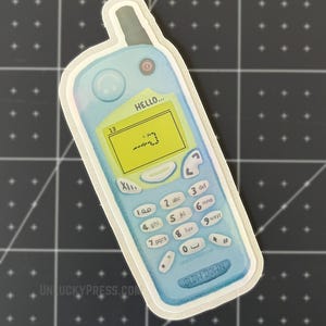 May include: A sticker of a retro blue cell phone with a screen displaying a pixelated snake game. The phone has a keypad with numbers and the text "HELLO..." above the screen. The sticker also has the text "SLOW DOWN" and "UNLUCKYPRESS.COM".