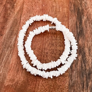 May include: A white shell necklace made of small, flat pieces of shell. The necklace is layered and has a silver clasp.