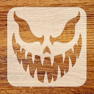 May include: A wooden square stencil featuring a carved, menacing jack-o'-lantern face. The design includes sharp, jagged teeth, curved eyebrows, and a triangular nose. The stencil is light-colored against a wood grain background, perfect for Halloween crafts.