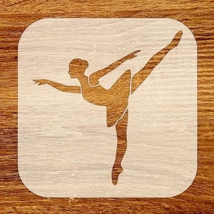 May include: A wooden stencil featuring a ballerina in a graceful pose. The dancer is depicted with one leg extended and arms outstretched, set against a light wood grain background. The design is cut out, creating a negative space effect.