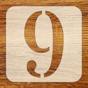 May include: A square stencil featuring a large, centered numeral nine with a classic serif typeface. The stencil is light beige with a smooth finish, showcasing the cut-out design of the number nine, which reveals the surface underneath.