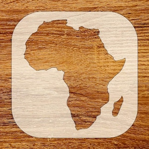 May include: A wooden stencil featuring the outline of the African continent. The stencil is light-colored and set against a warm, brown wood grain background. The design is enclosed within a rounded rectangular frame.