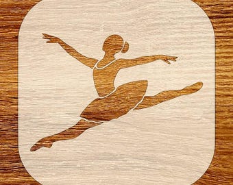 May include: A wooden stencil featuring a ballerina in mid-air, arms outstretched and leg extended. The dancer is depicted in a leotard and tutu. The stencil is set against a light wood grain background, with rounded corners.