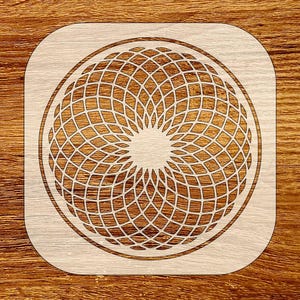 May include: A light-colored wooden stencil with a geometric design. The design features a circular pattern of intersecting lines, creating a symmetrical, web-like appearance. The stencil has rounded corners and is set against a wooden background.