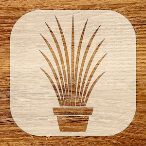 Puede incluir: Posavasos de madera con diseño de planta. El posavasos tiene un fondo de madera clara con forma cuadrada y esquinas redondeadas. La ilustración de la planta es de madera más oscura, que representa una planta en maceta con hojas largas y delgadas.