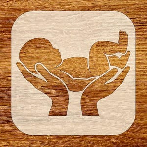May include: A wooden cutout featuring a baby cradled in two hands. The baby is in a fetal position, and the hands are cupped to support the baby. The cutout is light-colored, and the background is a wood grain pattern.