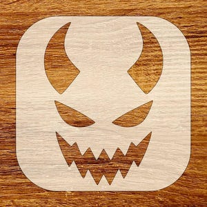 Puede incluir: Un esténcil cuadrado de color claro con una cara de diablo estilizada con cuernos, ojos angulados y una sonrisa con dientes de sierra. El diseño está recortado, creando un efecto de espacio negativo, ideal para manualidades y decoraciones de Halloween.