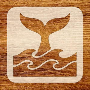 May include: A stencil featuring a whale tail emerging from ocean waves. The design is enclosed within a square frame with rounded corners. The stencil is white, set against a wood grain background.