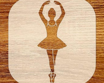 May include: A stencil featuring a ballerina in a graceful pose, arms raised above her head. The ballerina is wearing a tutu and pointe shoes. The stencil is cut from a light-colored material, set against a wooden background.