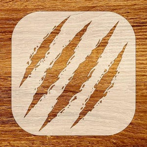 May include: A square wooden stencil with rounded corners showing four claw marks. The claw marks are cut out, revealing the wood grain beneath. The stencil is light-coloured, and the claw marks are a darker brown.