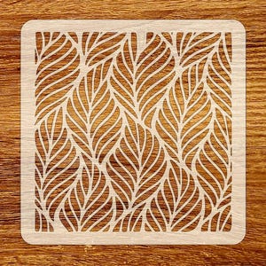 May include: A square, light-colored stencil with a repeating leaf pattern. The design features stylized leaves with curved lines, creating a textured effect. The stencil is made of a light-colored material, possibly wood or plastic, and is suitable for various craft projects.