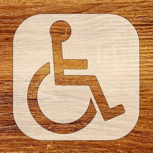 May include: A light-colored wheelchair symbol within a rounded square frame. The symbol is a stylized figure in a wheelchair, with a circular head and a curved lower portion representing the chair's wheel. The background is a wood grain pattern.