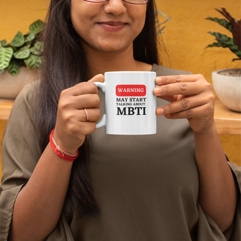 May include: White ceramic mug with a red warning sign that says "WARNING MAY START TALKING ABOUT MBTI".