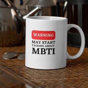 May include: White ceramic mug with a red warning sign that says "WARNING MAY START TALKING ABOUT MBTI".
