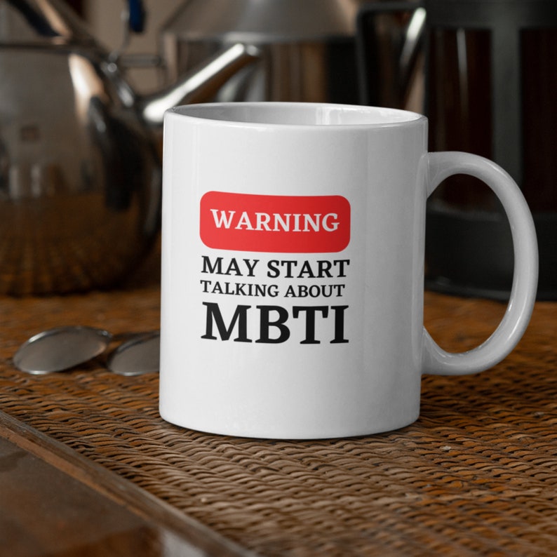 May include: White ceramic mug with a red warning sign that says "WARNING MAY START TALKING ABOUT MBTI".