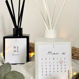 May include: Two glass diffuser bottles with black and white reeds. The black bottle has a label with the text "06:45 02.01.2022 Perine". The white bottle has a label with the text "Mai 2022" and a calendar with a heart on the 6th.
