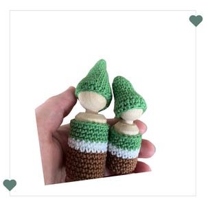 Puede incluir: Dos muñecos de gnomo de crochet con sombreros verdes y cuerpos rayados marrones, blancos y verdes.
