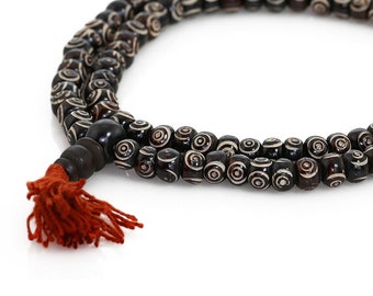 May include: A black and white mala prayer bead necklace with a red tassel. The beads are made of bone and have a swirling pattern.