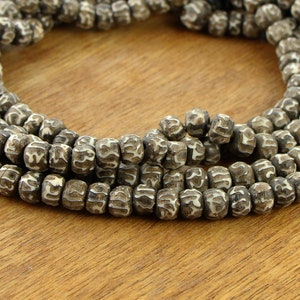 May include: A strand of brown wooden beads with white lettering. The beads are round and have a slightly textured surface.