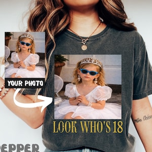 May include: Dark gray t-shirt with a photo of a young girl wearing a crown and sunglasses. The text "LOOK WHO'S 18" is printed in gold. The word "PEPPER" is printed in a retro font.
