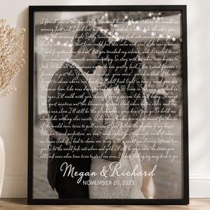 May include: A black and white framed print featuring a couple embracing, overlaid with white cursive text of song lyrics. The bottom displays the names Megan & Richard and the date November 10, 2023, in a clean, white serif font.