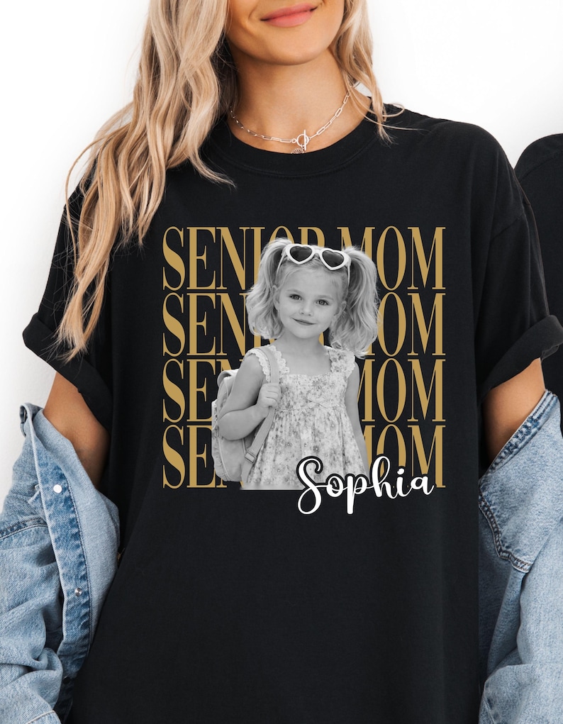 Pu&ograve; includere: Una t-shirt nera a maniche corte con una grafica dorata ripetuta che recita SENIOR MOM. Al centro &egrave; presente una fotografia in bianco e nero di una bambina con le codine, occhiali da sole a forma di cuore e uno zaino, con il nome Sophia.
