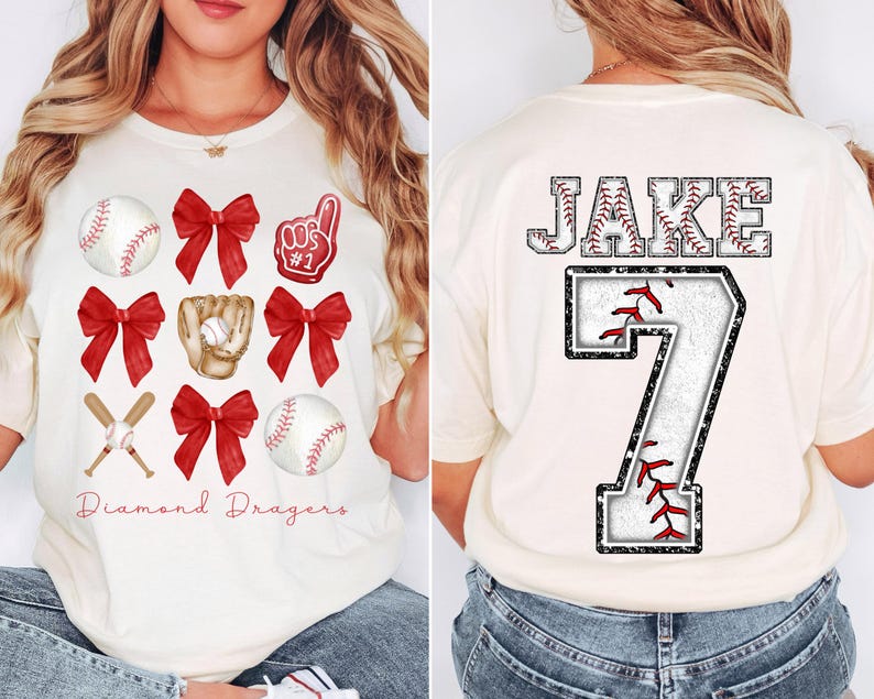 May include: White t-shirt with red and white baseball themed graphics. The front of the shirt has a baseball, bats, bows, and a glove. The back of the shirt has the name "JAKE" and the number "7" in a baseball-themed font.