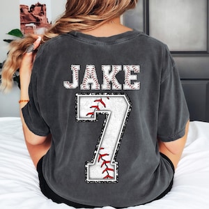 May include: A dark gray t-shirt with a white baseball design and the name "JAKE" and the number "7" printed on the back.
