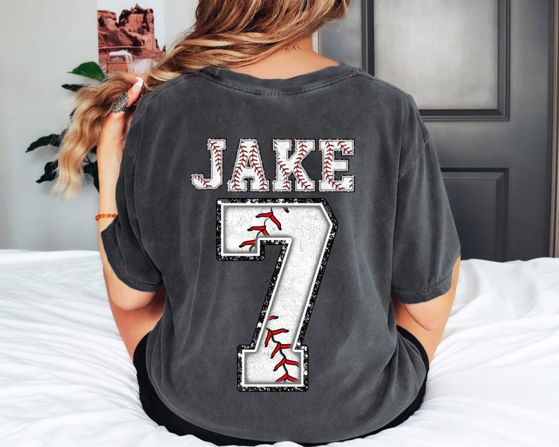 May include: A dark gray t-shirt with a white baseball design and the name "JAKE" and the number "7" printed on the back.