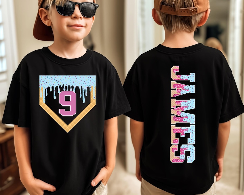 May include: Black t-shirt featuring a baseball home plate design with a number 9 in pink. The top of the design has blue sprinkles and dripping icing. The back of the shirt has the name "JAMES" in a vertical design with donut-themed letters.