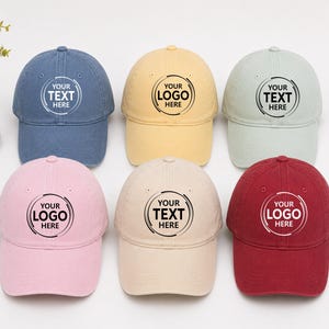 May include: Six baseball caps in blue, yellow, light green, pink, beige, and red. Each cap features a circular graphic with the text 'YOUR TEXT HERE' or 'YOUR LOGO HERE' printed in the center. The caps have a structured crown and a curved brim.