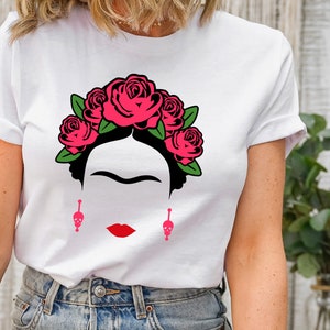 May include: White t-shirt with a black and white illustration of Frida Kahlo wearing a pink flower crown and skull earrings.