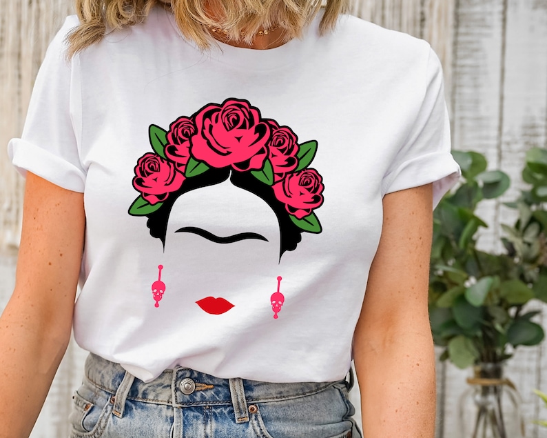 May include: White t-shirt with a black and white illustration of Frida Kahlo wearing a pink flower crown and skull earrings.