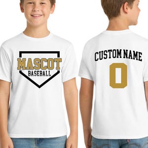 May include: White t-shirt with "MASCOT BASEBALL" in gold and black lettering on the front. The back of the shirt features "CUSTOM NAME" above a gold number 0. The shirt is worn by a person.